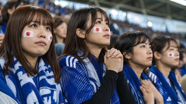 スタジアムで日本代表を祈るように応援する青いユニフォーム姿の日本人女性サポーターたち
